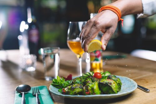 En hånd klemmer sitronsaft over grillet kjøttretter, med et glass vin i bakgrunnen.